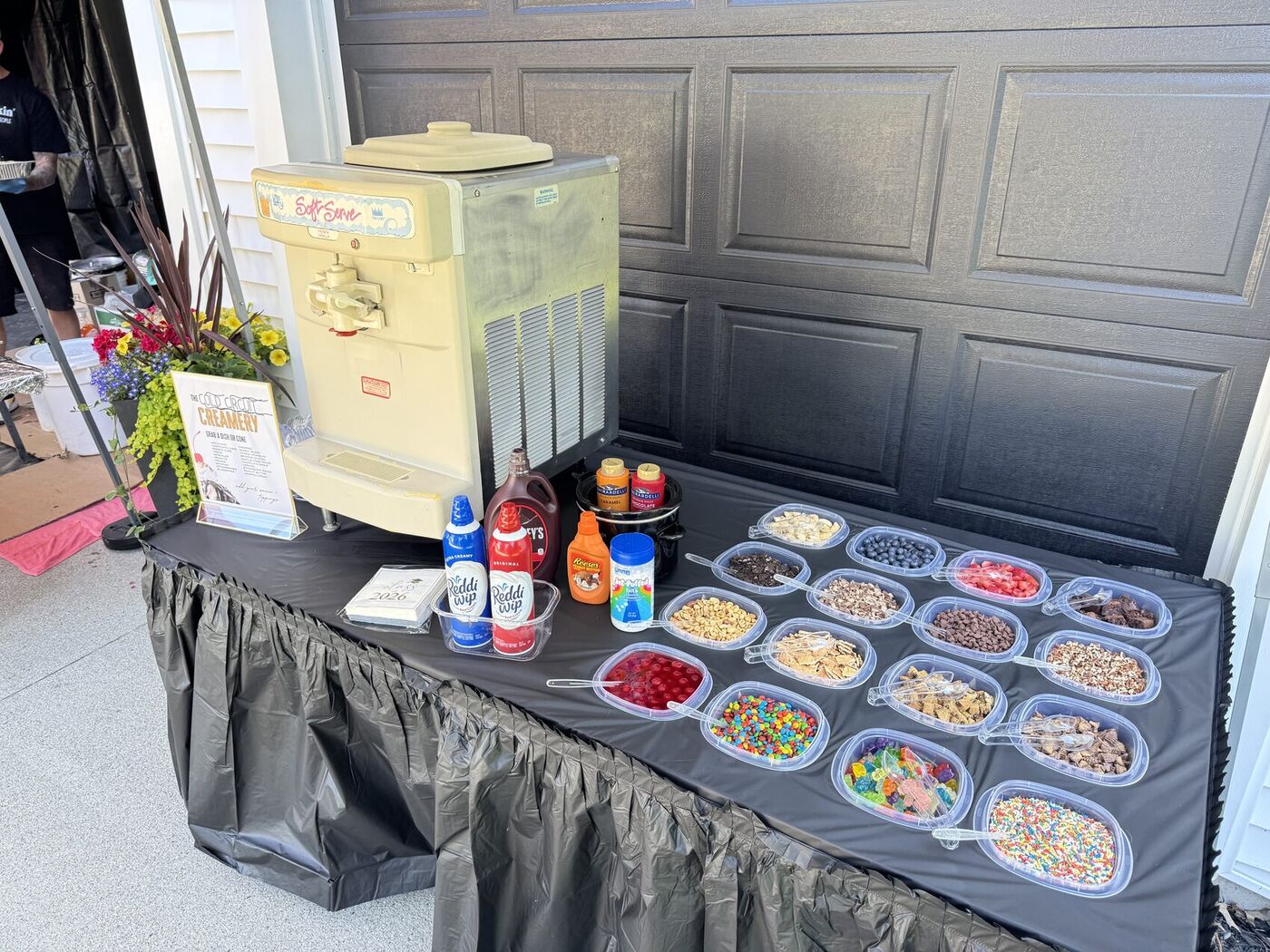 Sundae bar display with soft-serve machine, syrups, and rows of toppings