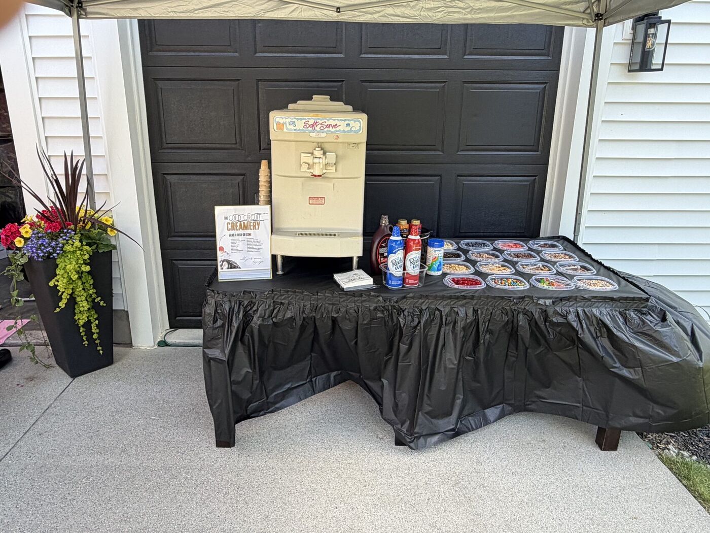 Event display table set up as a sundae bar with a soft-serve machine and toppings under a tent
