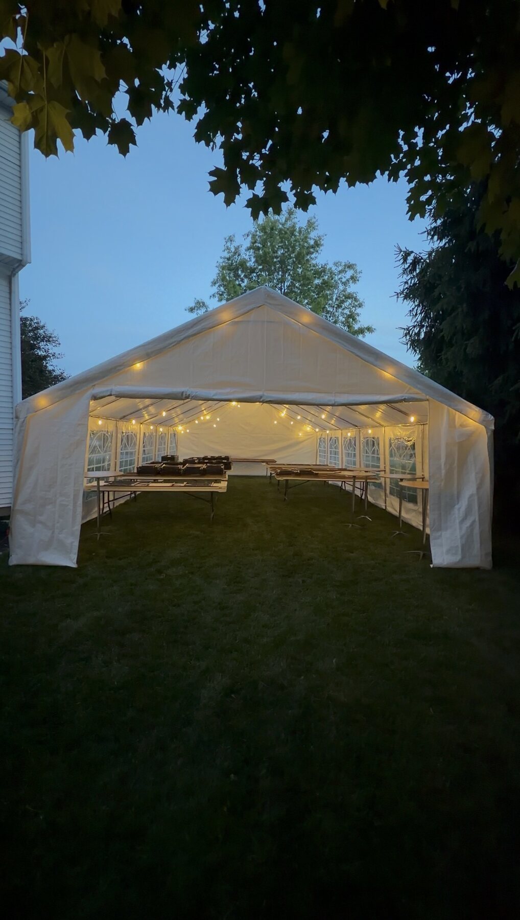 20x40 white frame event tent set up in a backyard at dusk with string lights glowing inside